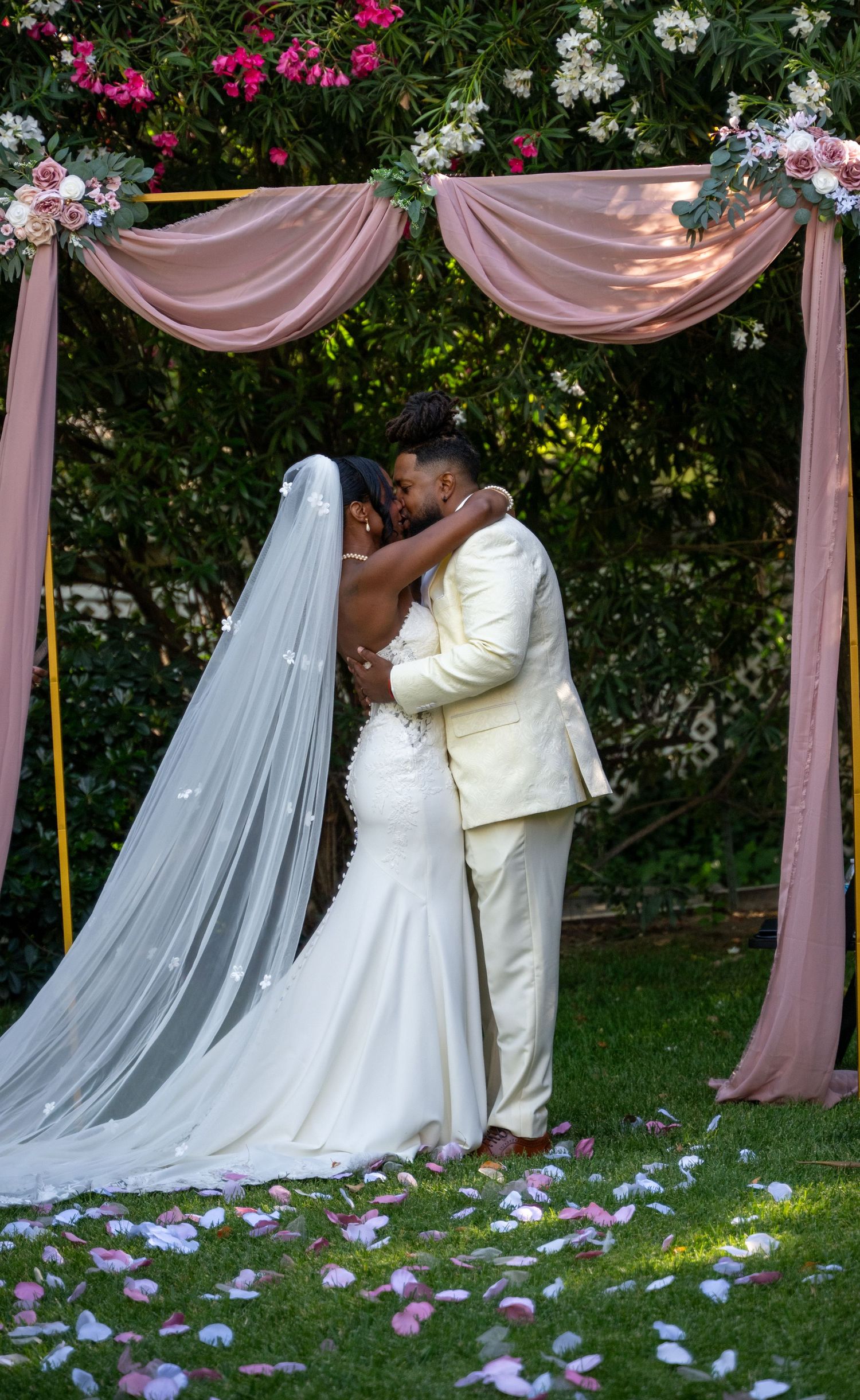 A couple shares a romantic moment under pink drapery during their garden wedding ceremony.