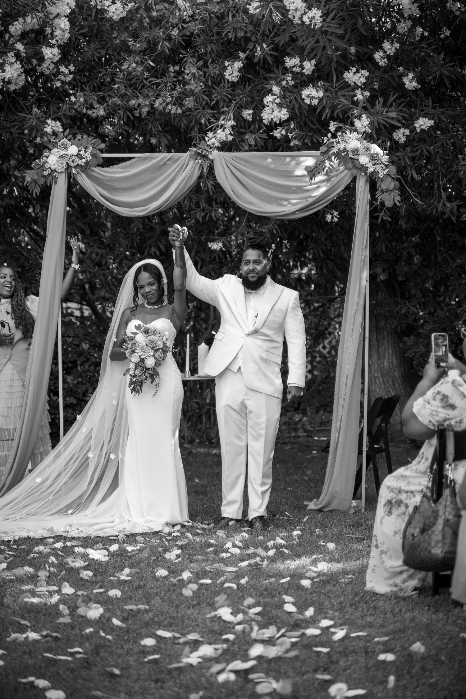 A black and white photo of a couple celebrating during their outdoor wedding ceremony.