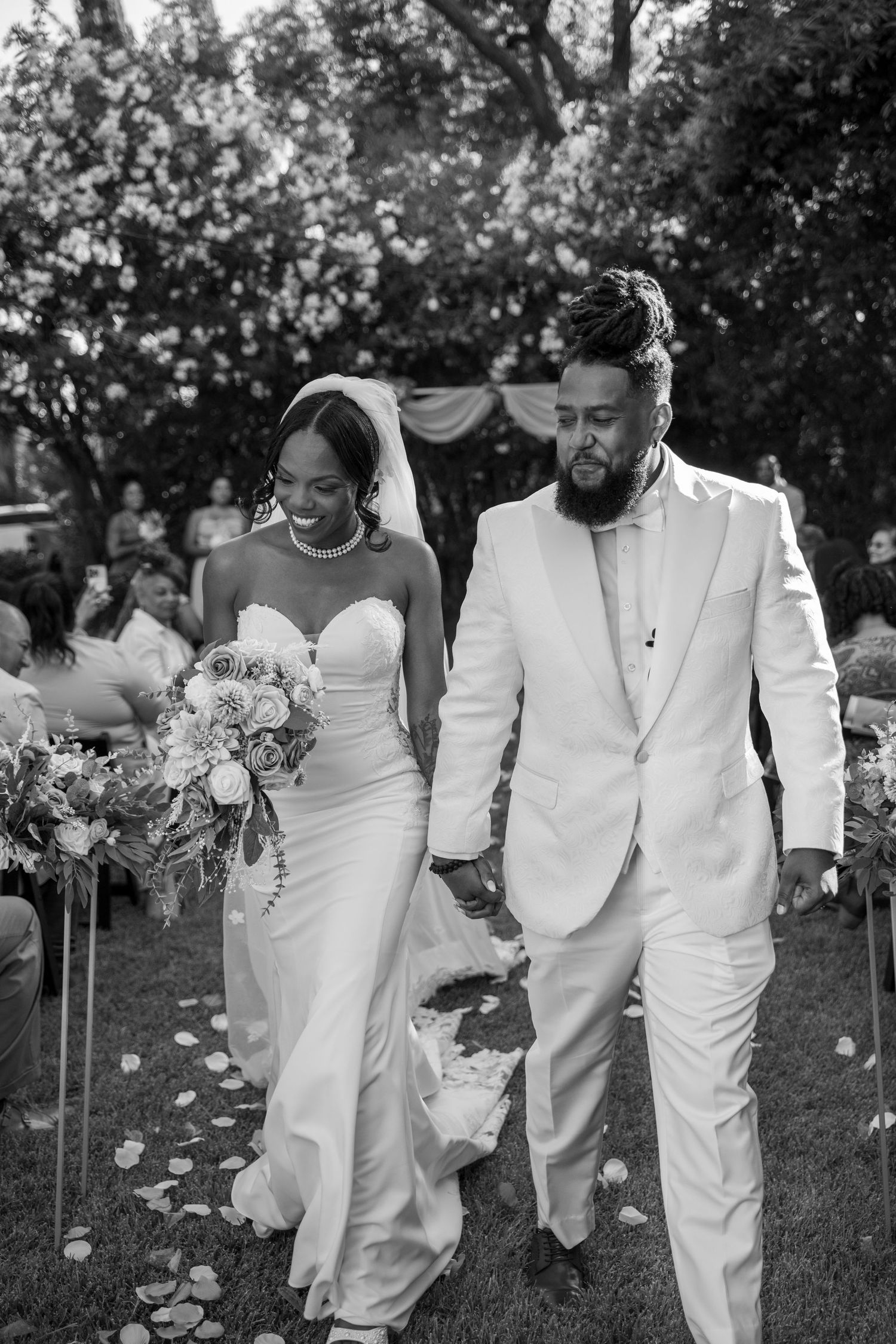 A black and white photo of a couple walking together during their garden wedding.