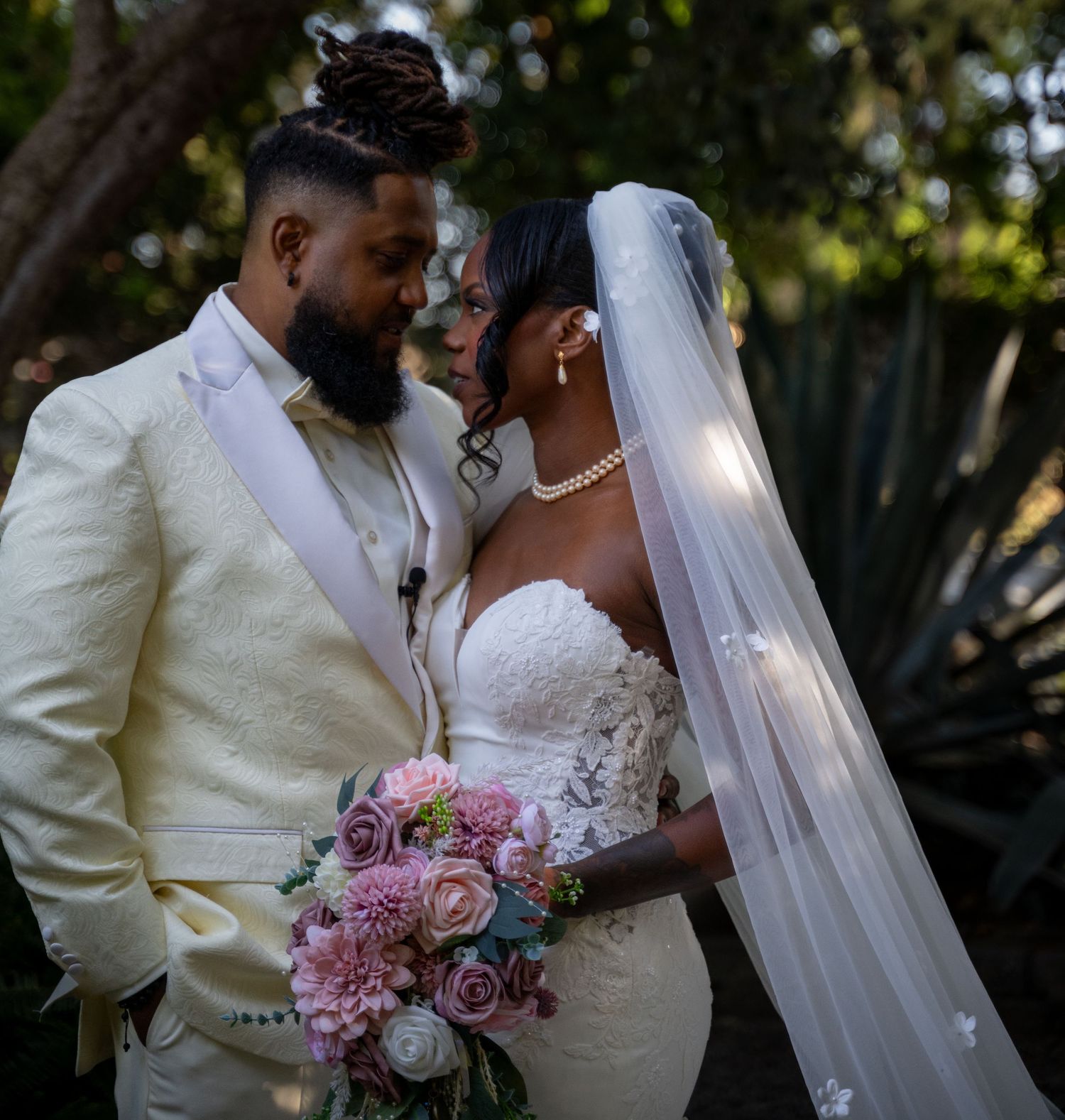 A couple in white wedding attire shares intimate moments in a garden setting.