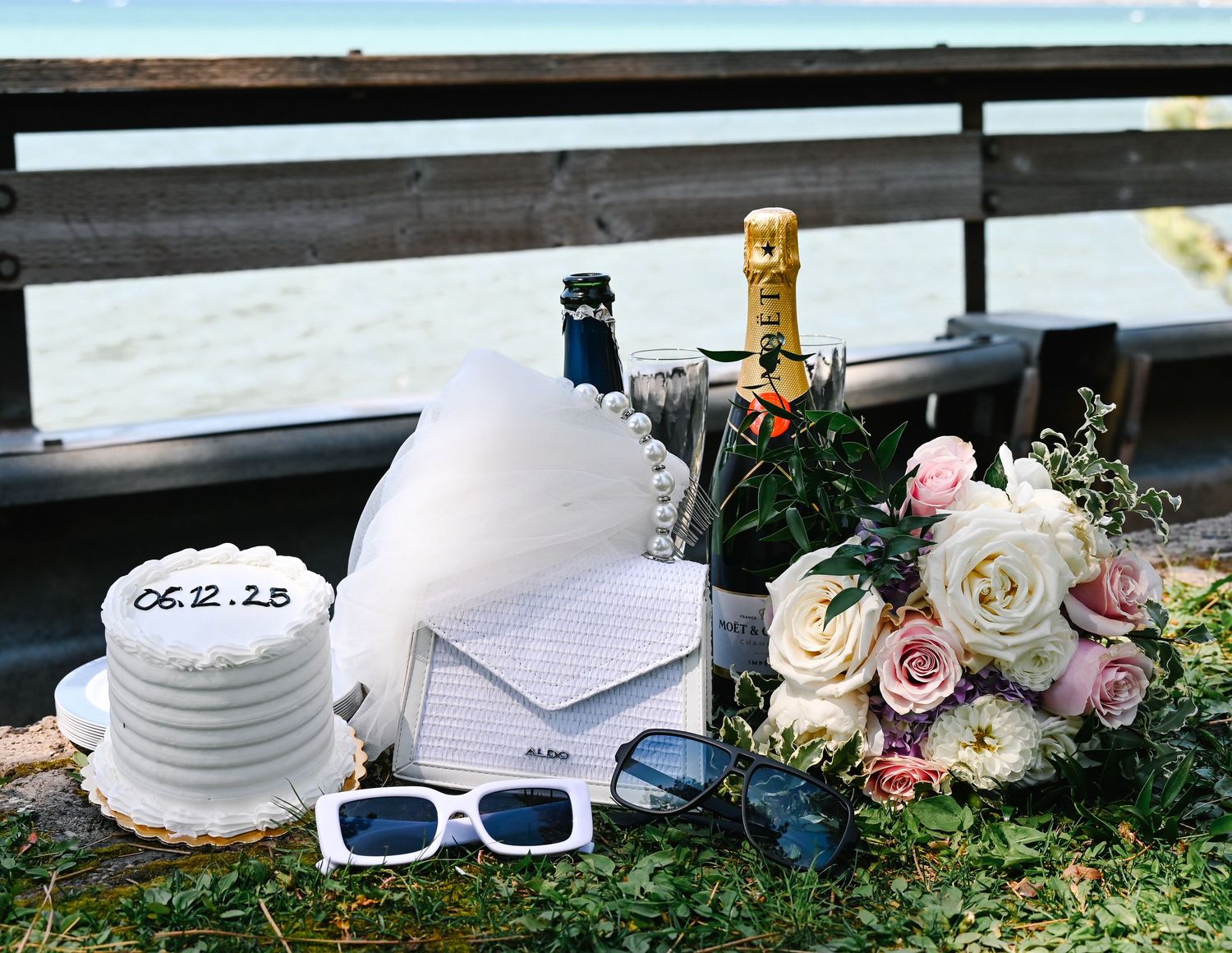 A collection of white sunglasses, sun hats, and delicate pink roses arranged on grass create a dreamy summer aesthetic.