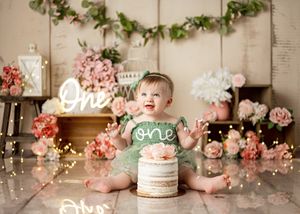 Cake smash photo collage with pink flowers, rustic background, and glowing 'one' sign for first birthday celebration.