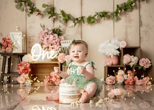 Elegant cake smash photo setup with pink flowers, greenery garland, and rustic backdrop for a special celebration.