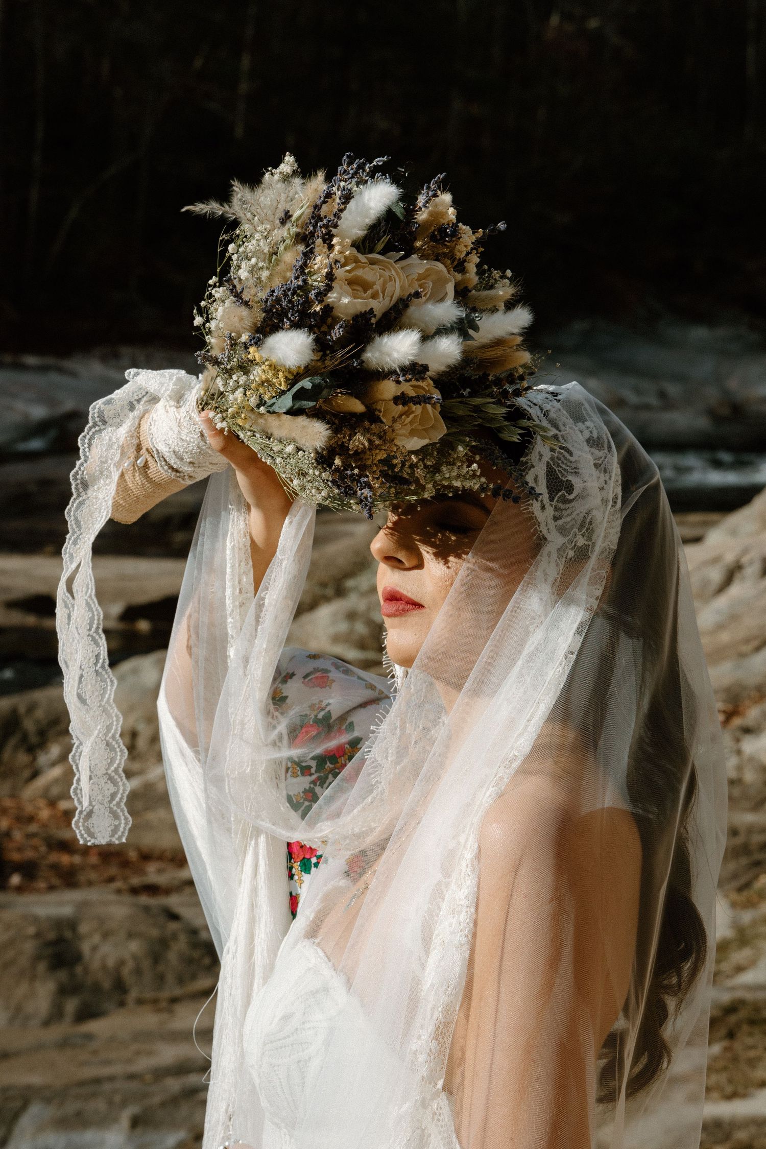 Dreamy bridal portrait showing delicate lace veil and floral crown against dark moody background in autumn setting.
