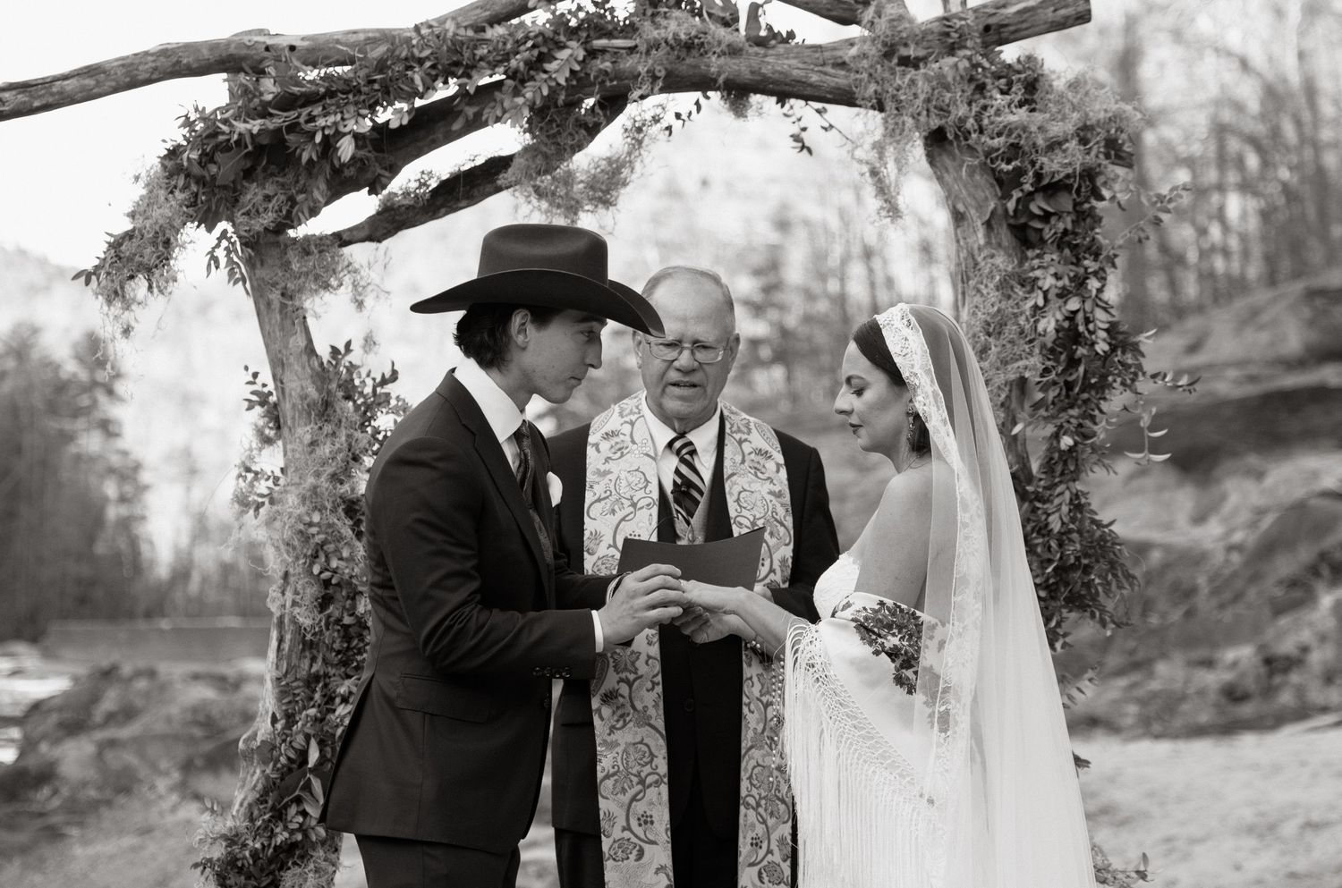 Four black and white photos show joyful moments from a wedding ceremony with the couple and guests outdoors in a garden setting.