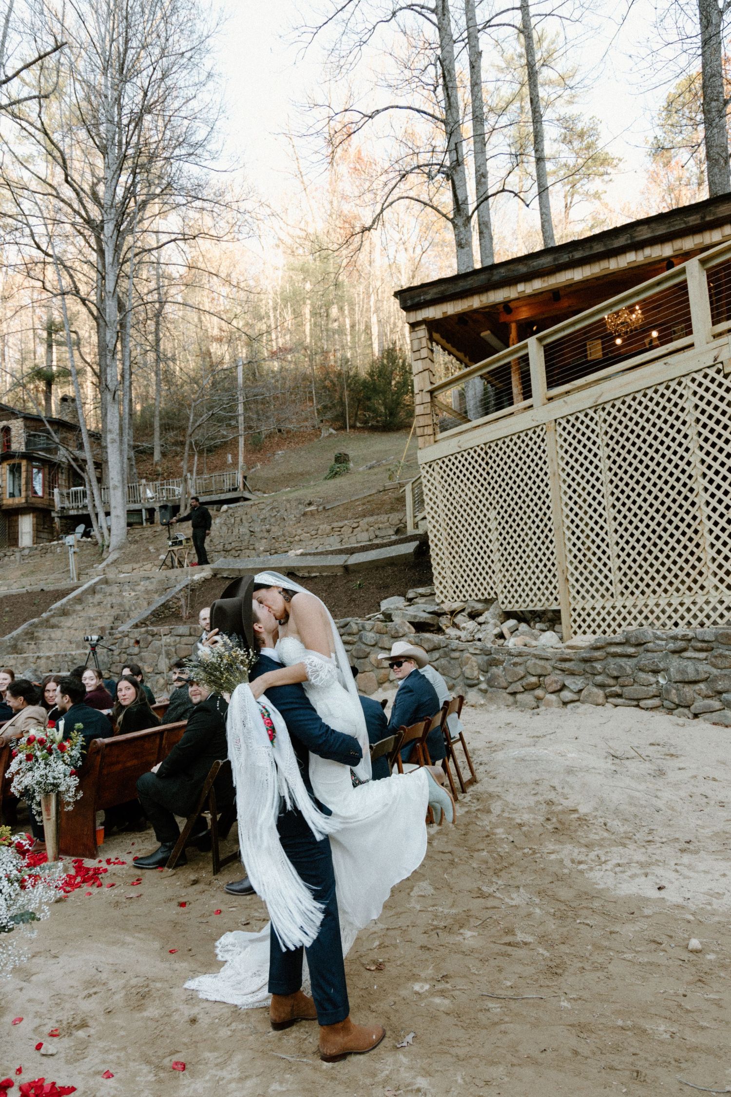 A couple performs a playful wedding dance routine in front of wooden decking and trees in an outdoor forest setting.