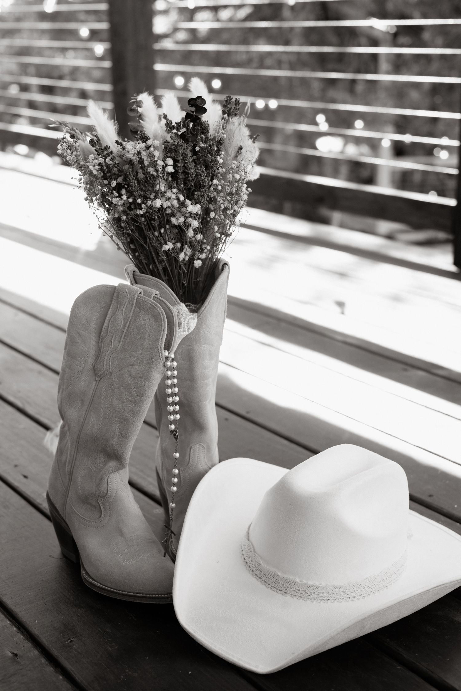 White cowboy boots and hat displayed on wooden table with dried flowers creating a rustic western aesthetic arrangement.