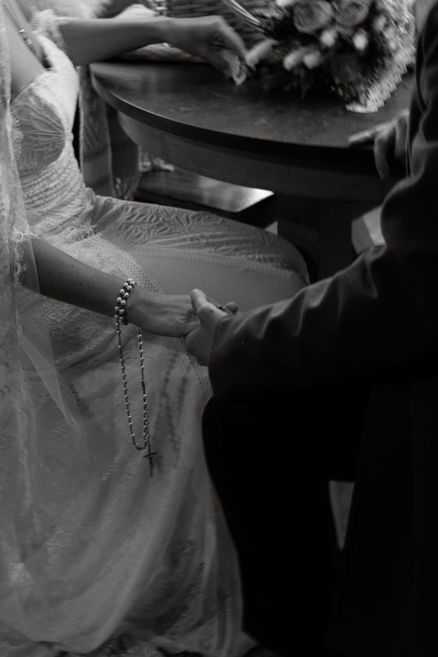 A person wearing a rosary and white dress holds their hands together in what appears to be a prayer position.
