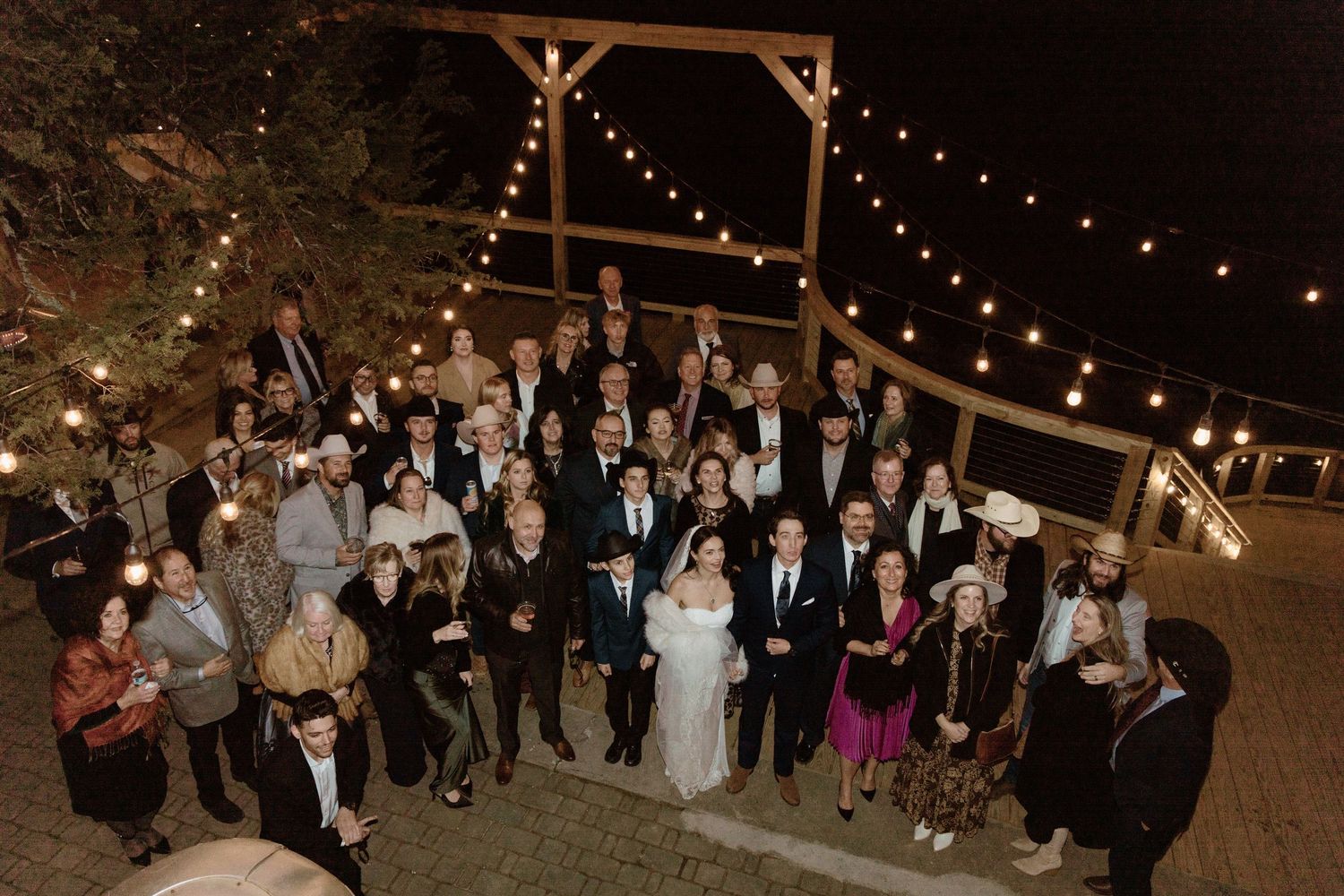 Wedding guests dance together under glowing string lights at an outdoor rustic reception venue.