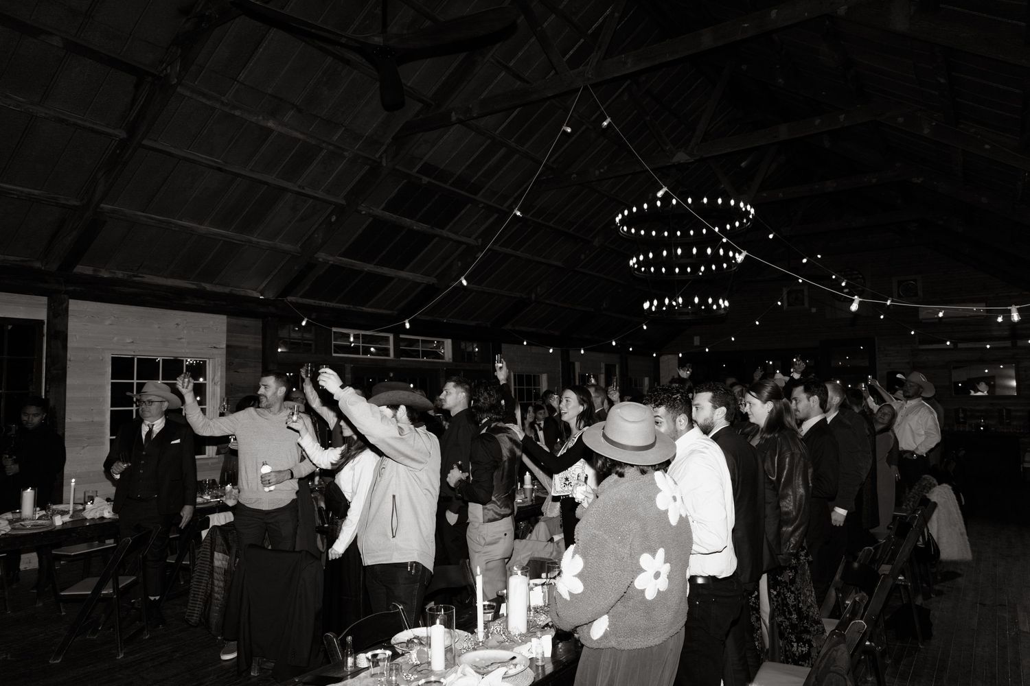 People dancing and socializing at a nighttime indoor event with hanging lights and decorations in black and white.