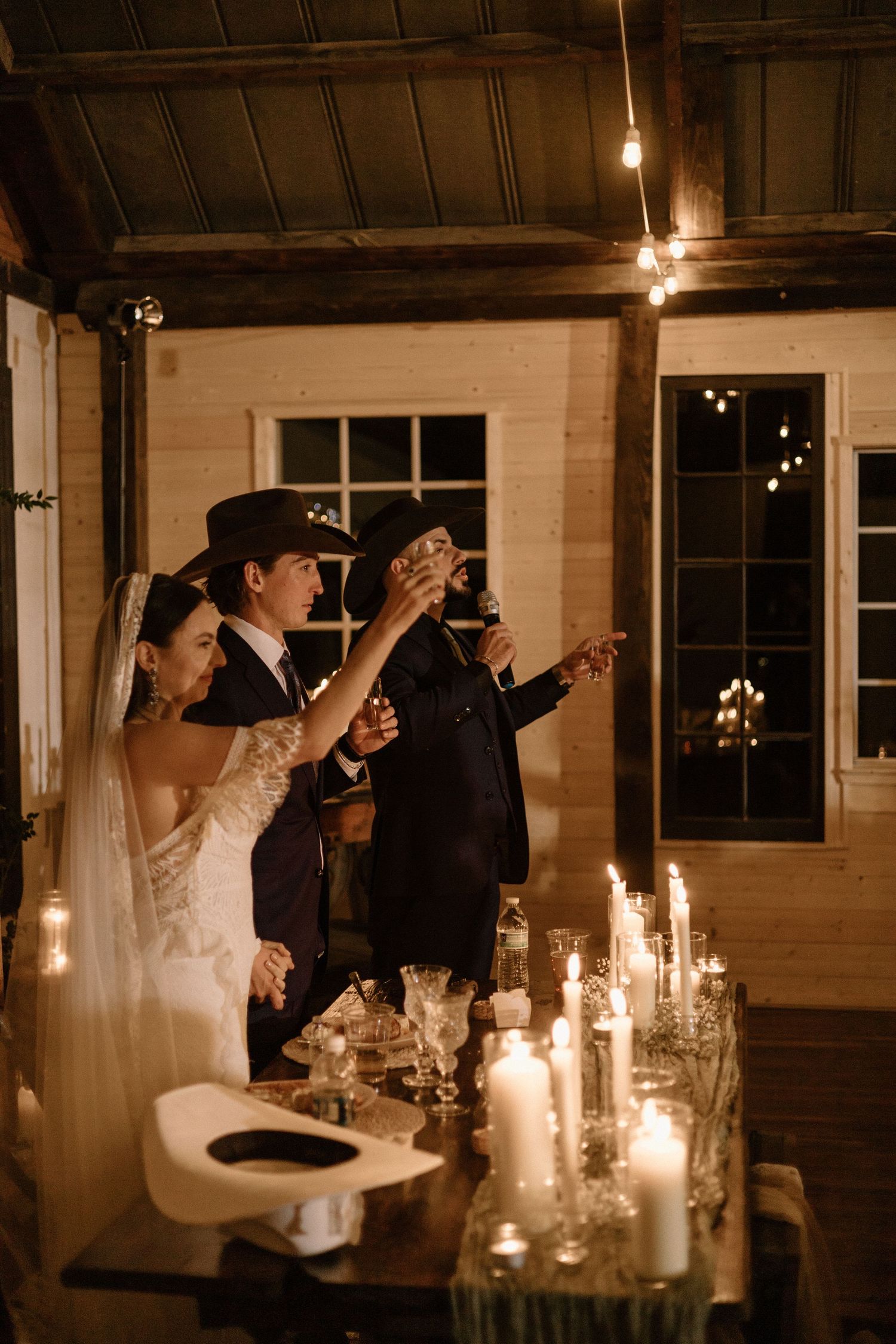 A romantic wedding reception scene with couples sharing intimate moments at a candlelit table in a rustic venue.