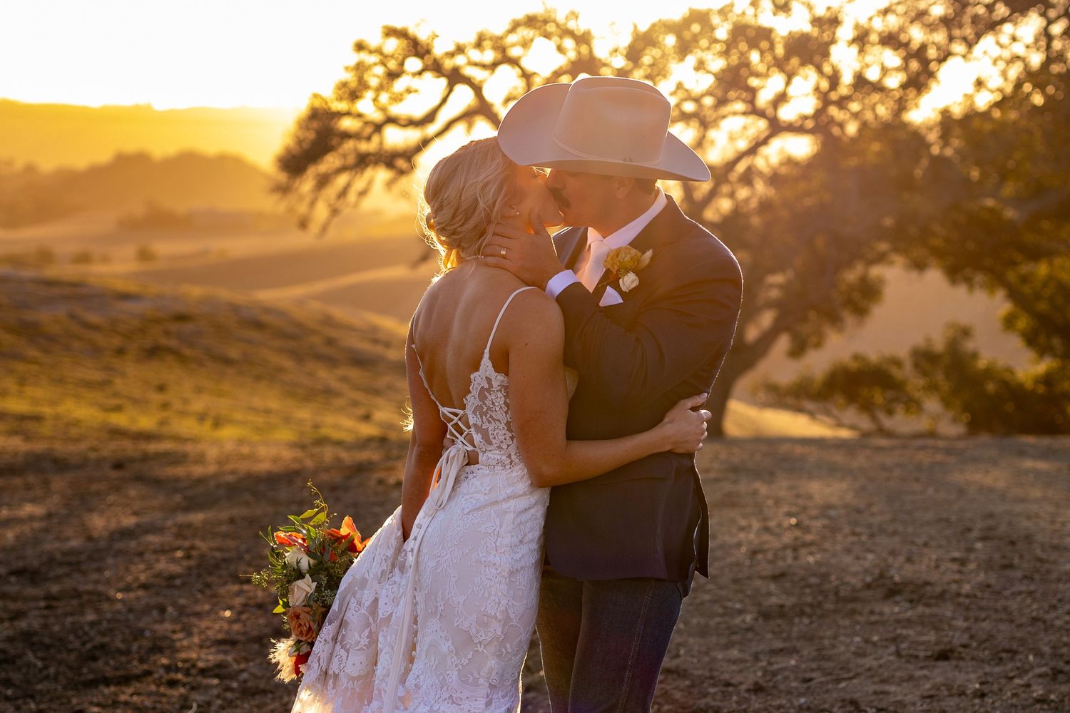 Silhouettes stand together on a dirt path as golden sunlight bursts through tree branches during sunset.