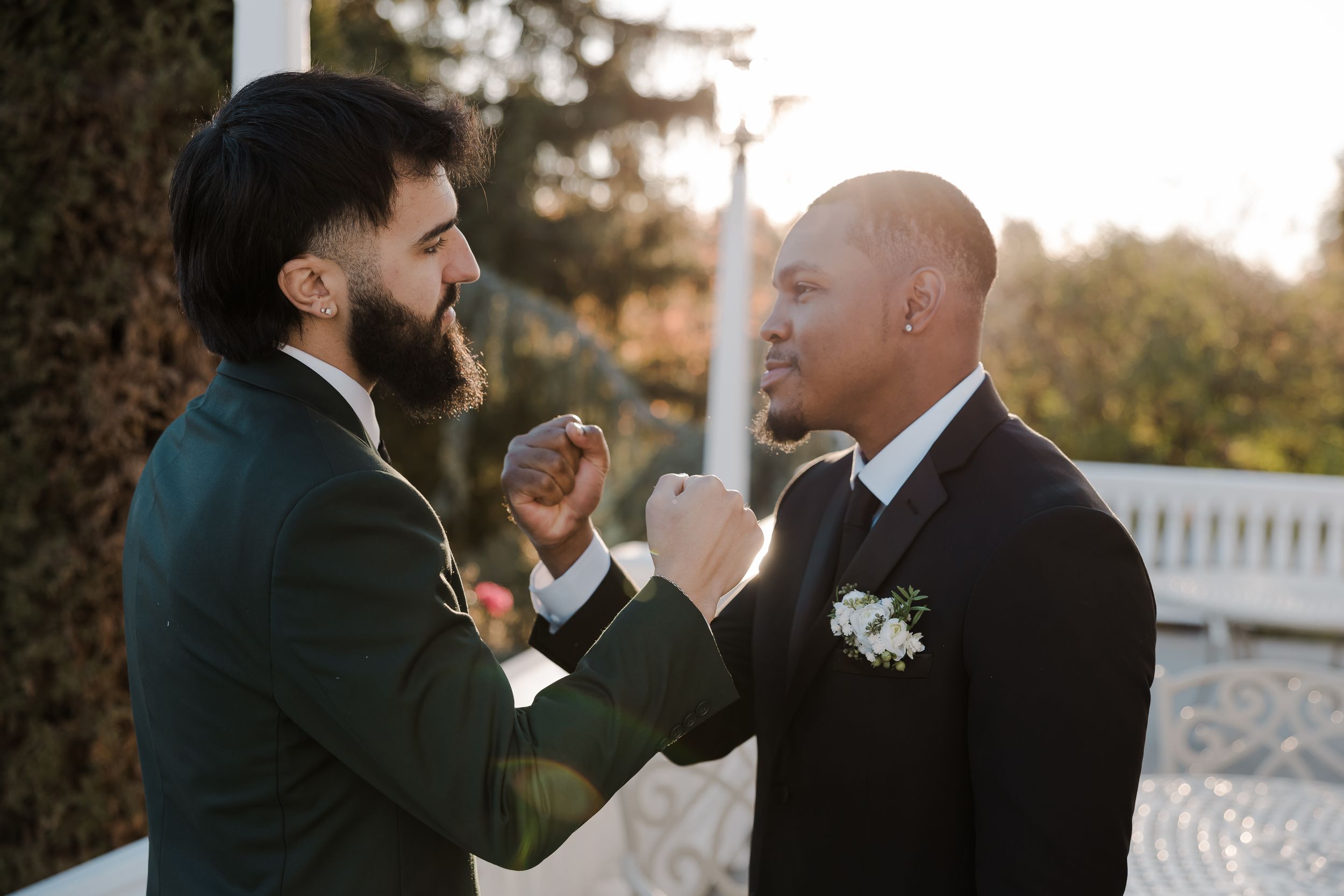 Two men in formal attire share a playful moment outdoors during golden hour at an event.