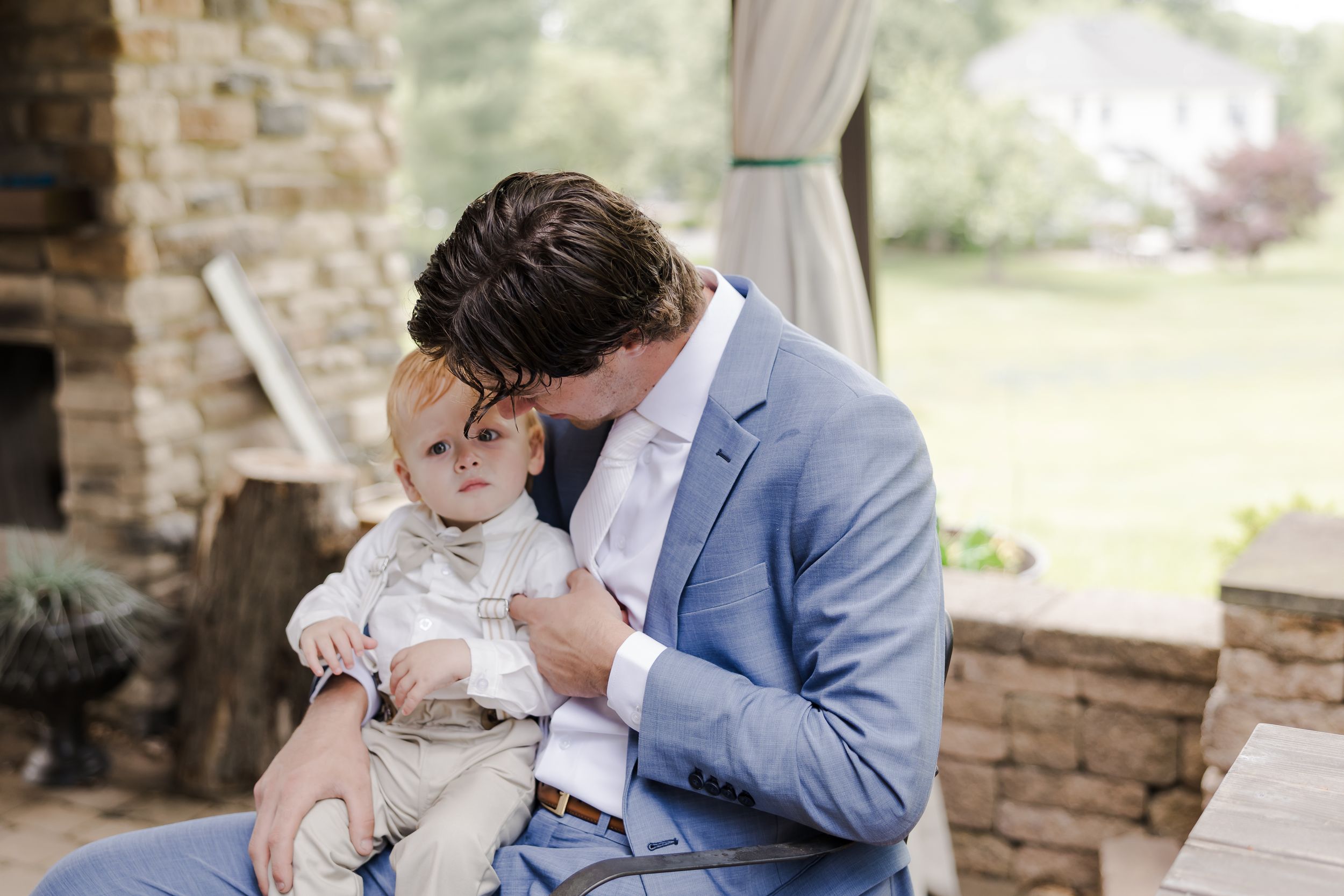 A tender moment on a porch with a baby in white clothing and a person wearing a light blue suit jacket.