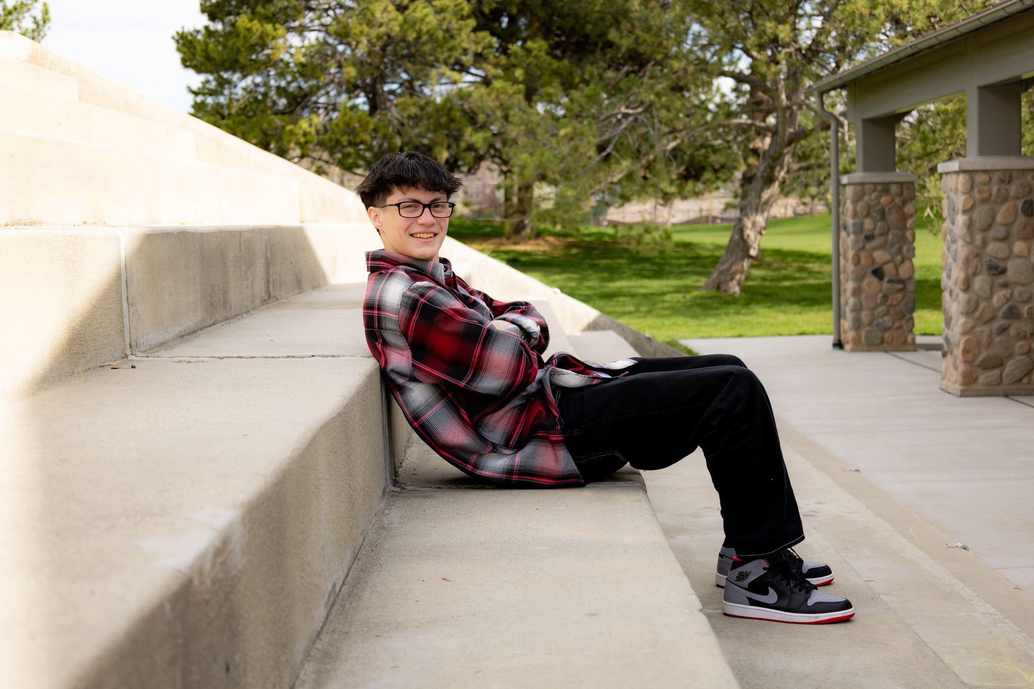 Graduate in red plaid shirt relaxing on concrete steps outdoors.