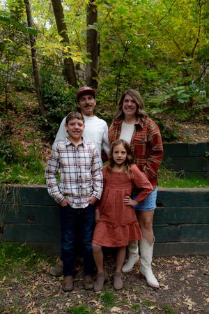 Family portrait against a rustic wooden wall surrounded by autumn leaves and greenery.