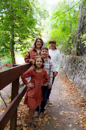 Playful autumn photoshoot along a stone-walled path with fallen leaves.