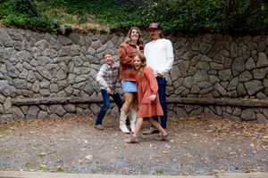 Casual outdoor family photos against a stone wall backdrop on a fall day.