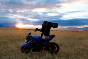 Motorcycle silhouetted against dramatic sunset sky over open grassland field.