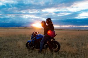 Blue motorcycle parked in golden field during sunset with dramatic clouds.