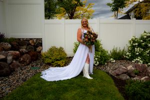 Wedding party poses against a white backdrop in a garden setting with green trees and rocks.