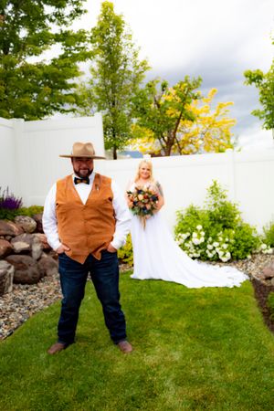 Rustic wedding attire featuring brown vests and white shirts against an outdoor garden backdrop.