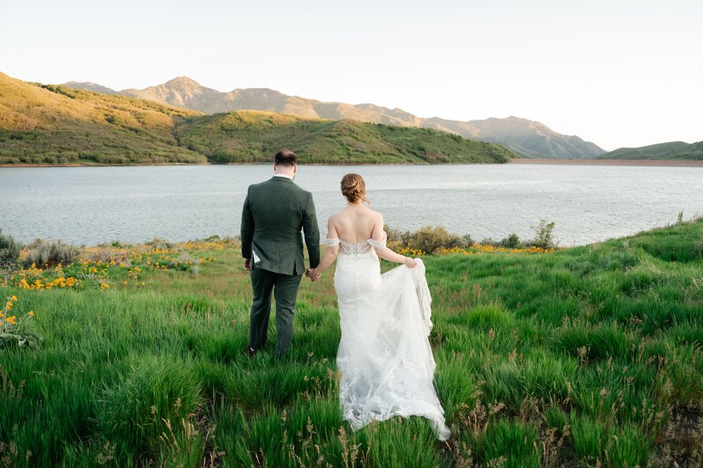 Bride and groom stand together overlooking serene mountain lake and green hillsides.