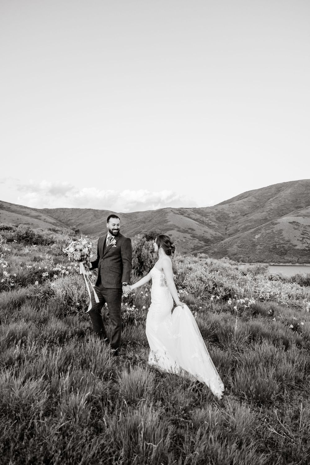 A bride and groom share a romantic moment on a grassy mountainside during their black and white wedding photoshoot.