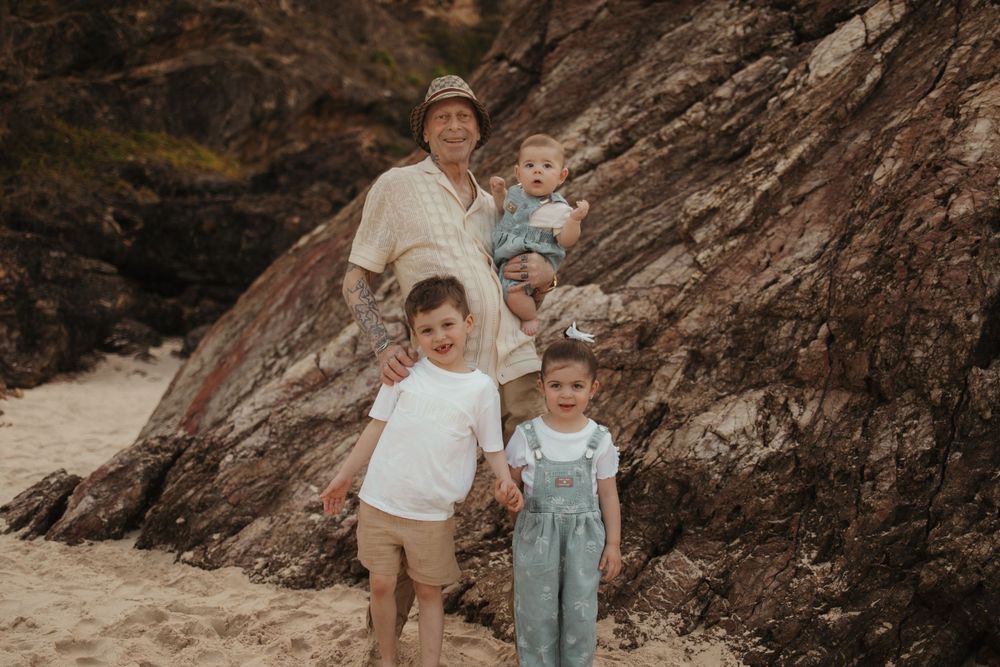 A family of four poses together against rugged rocky terrain at sunset wearing casual white and denim outfits.