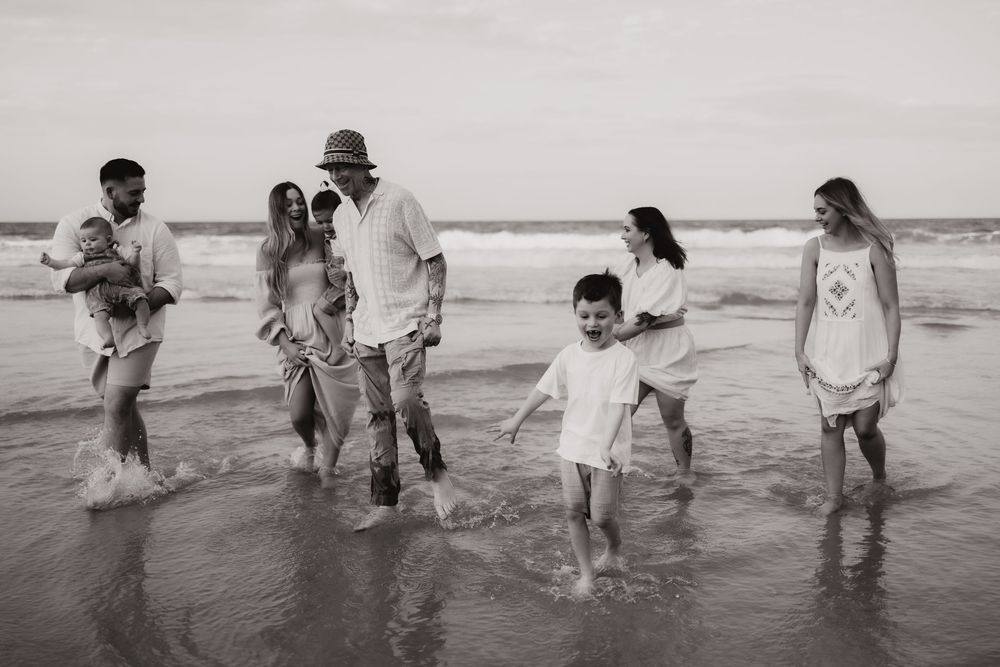 Black and white panoramic photo sequence showing people enjoying a day playing in the ocean waves at the beach.