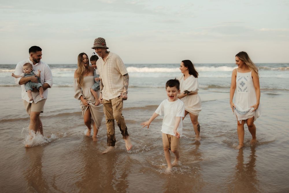 Group in light colored clothing walking and splashing together along the beach shoreline at sunset.