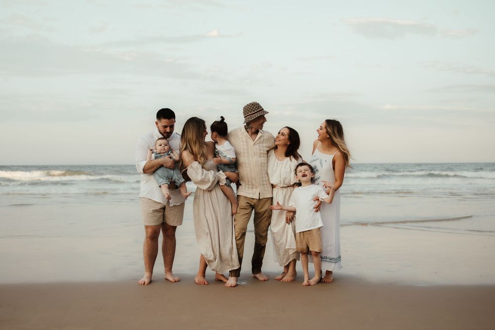 Group in white and beige clothing walking and posing together on a sandy beach at sunset.