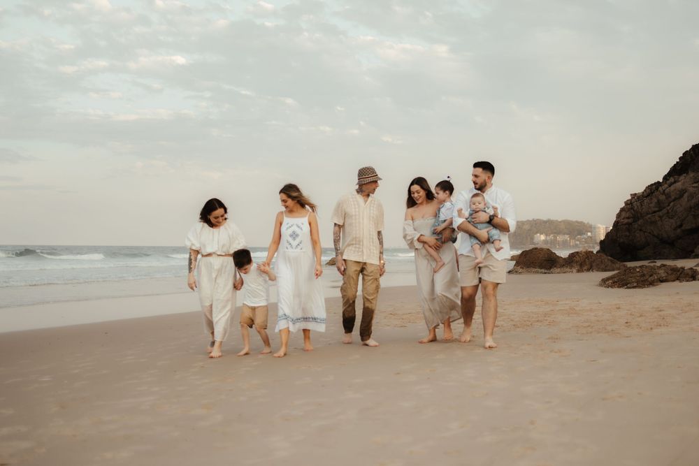 A group in white clothing walks together along a scenic beach with cliffs and ocean waves at sunset.