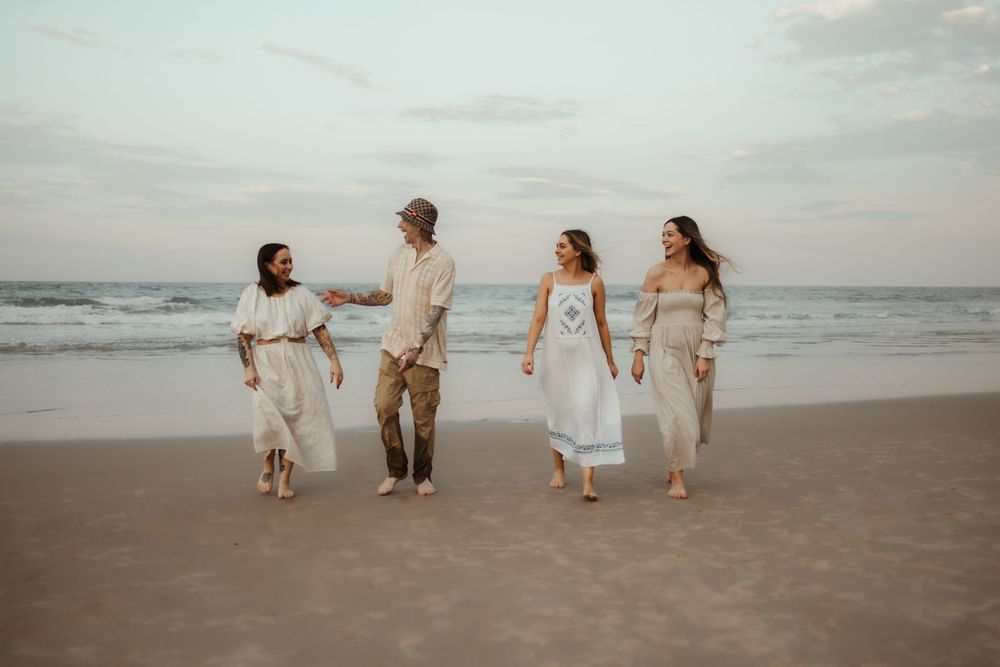 Group walking together on a serene beach at sunset wearing light colored casual beach attire.
