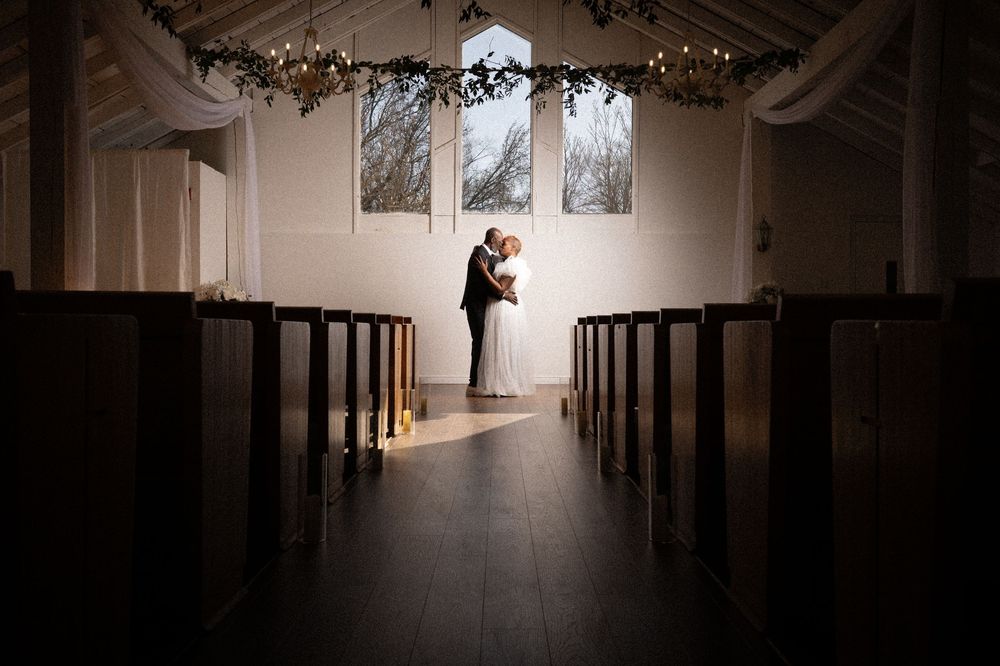 Dimly lit church interior with wooden pews and decorative lights strung along the ceiling creating an intimate atmosphere.