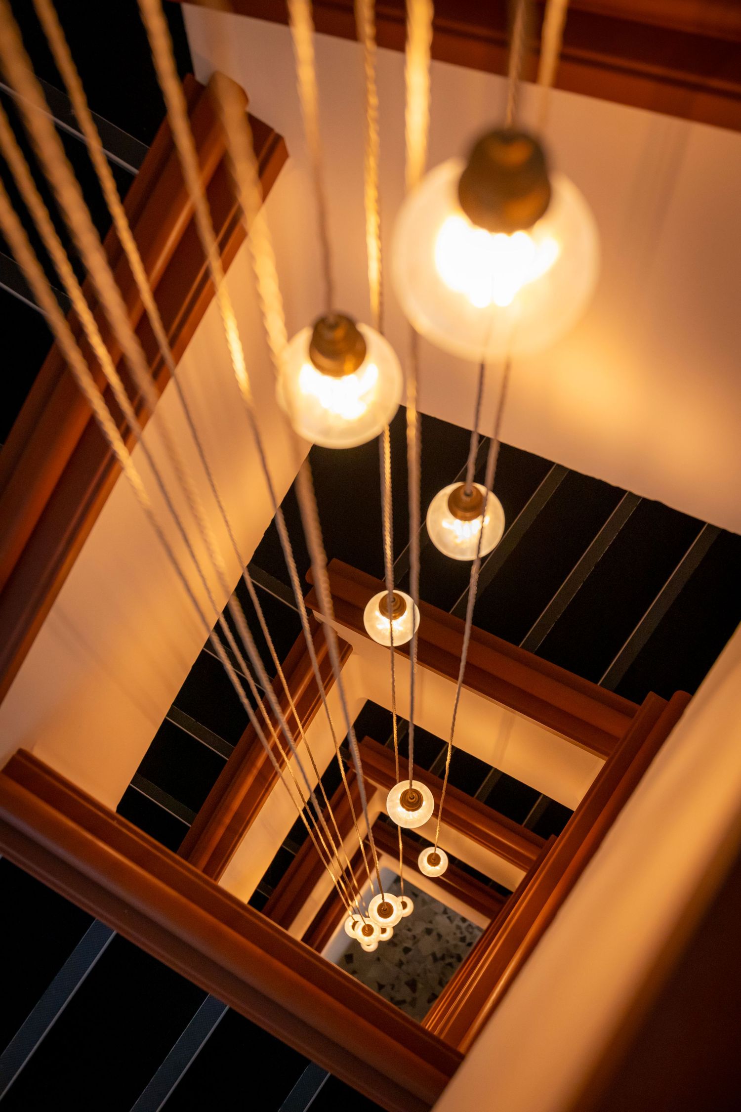 Warm pendant lights spiral down a staircase with golden ropes.