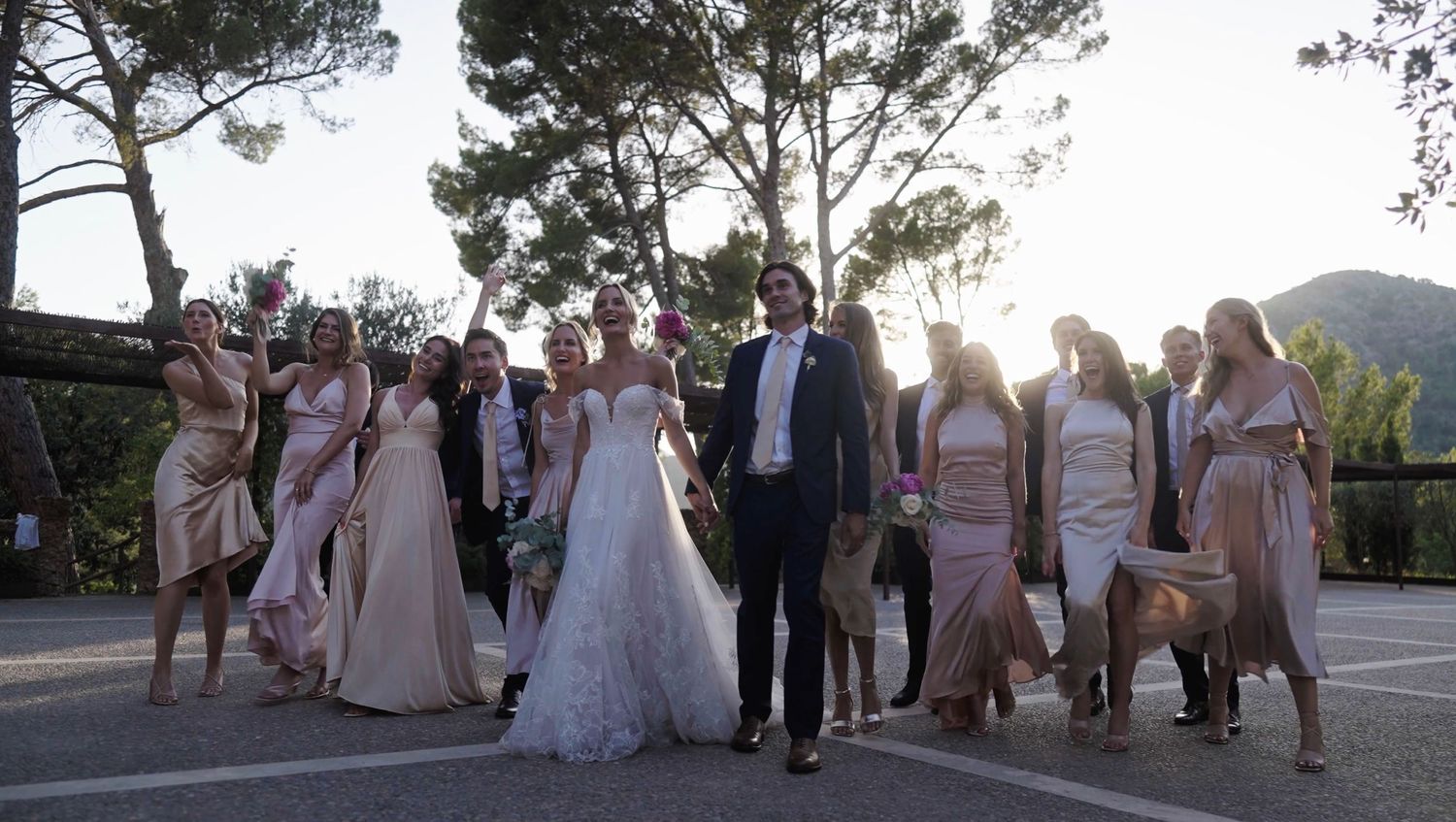 Bride and groom walking with their wedding party at sunset, surrounded by bridesmaids in pastel dresses.