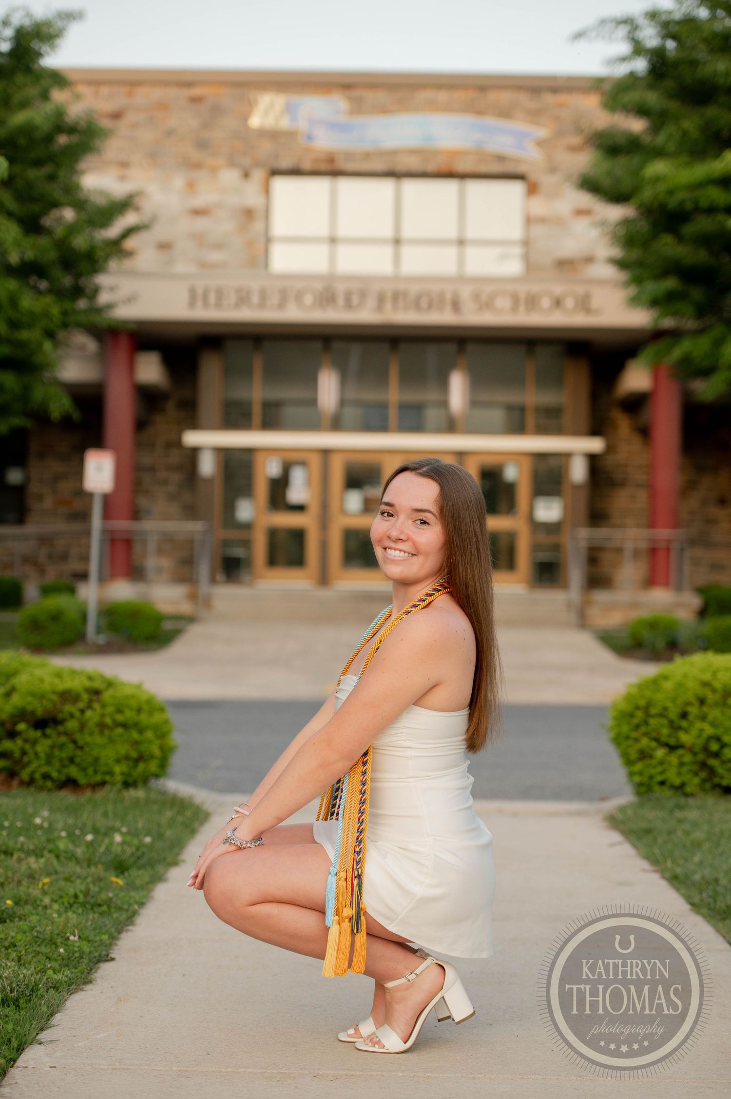 A student poses in a white dress outside Heritage Middle School's entrance on a sunny day.