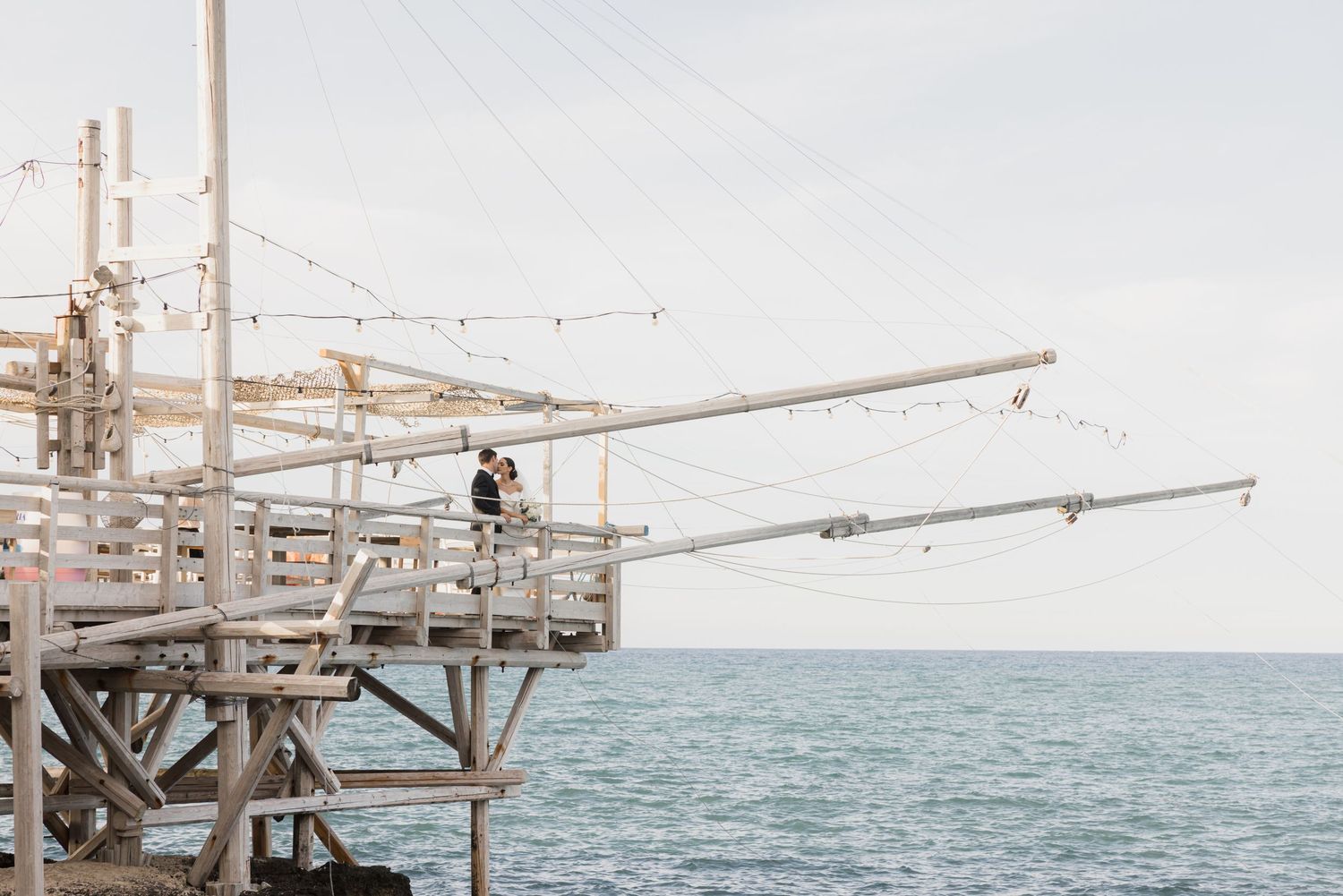Scenic oceanfront venue with wooden pier and string lights at sunset.