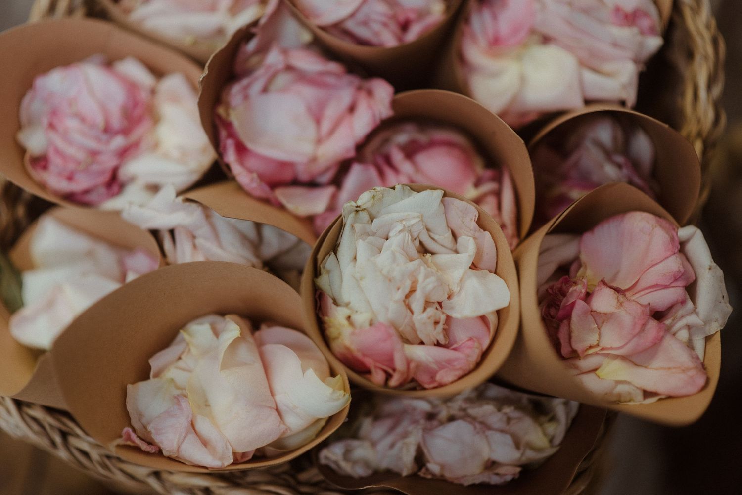 Pink and white peony petals arranged in terracotta pots within a woven basket.