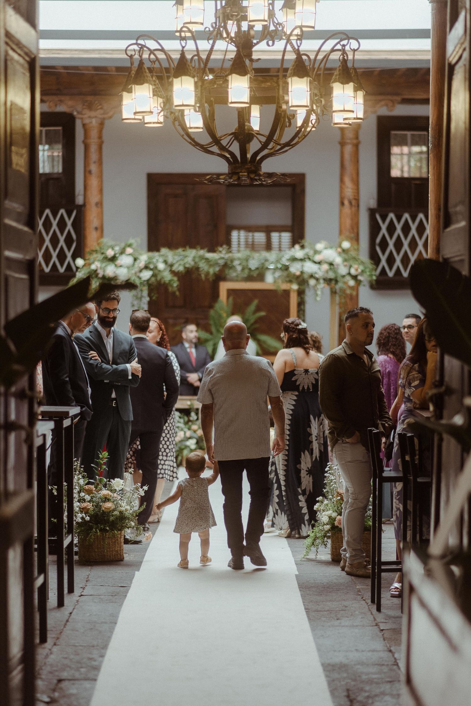 A wedding ceremony aisle decorated with white flowers and an elegant chandelier in a vintage indoor venue.
