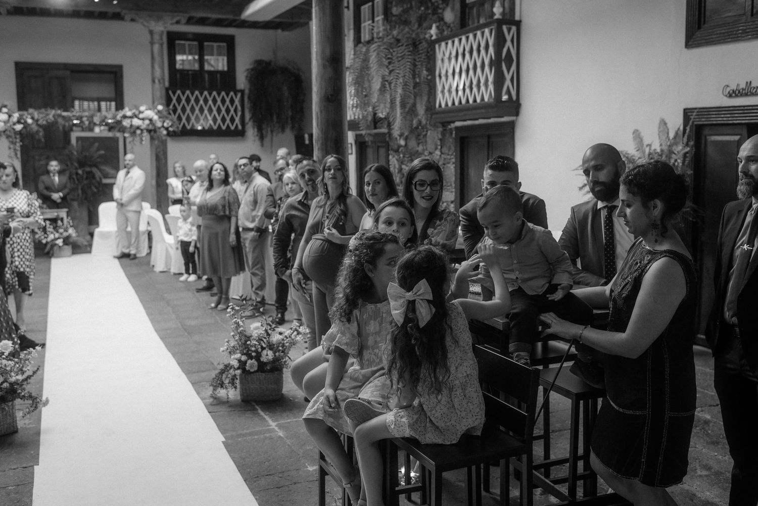 Wedding ceremony guests seated in rows along white aisle runner in elegant indoor venue with chandeliers.