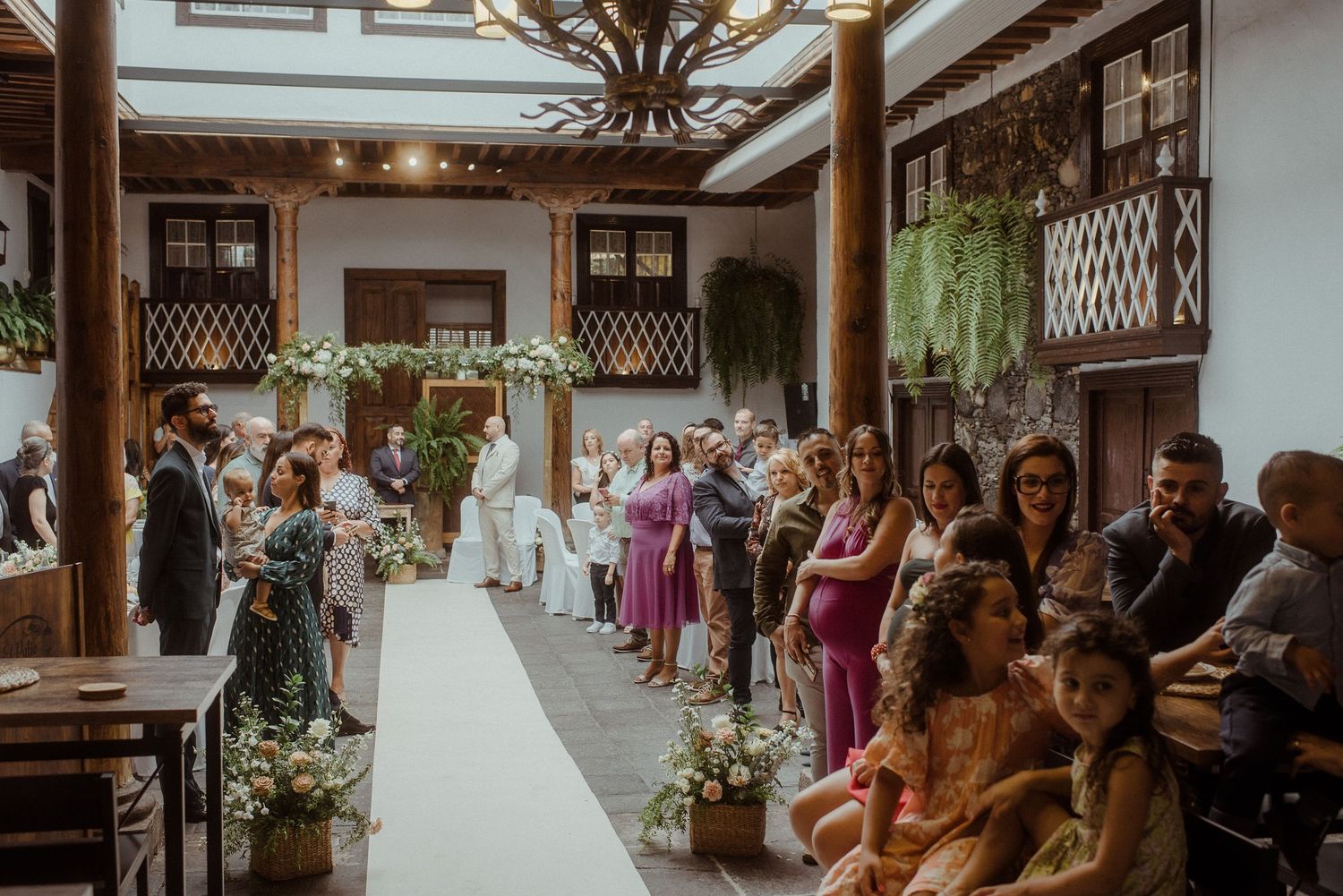 Wedding guests seated in rows watch as a bride walks down a rustic wooden aisle during an indoor ceremony.