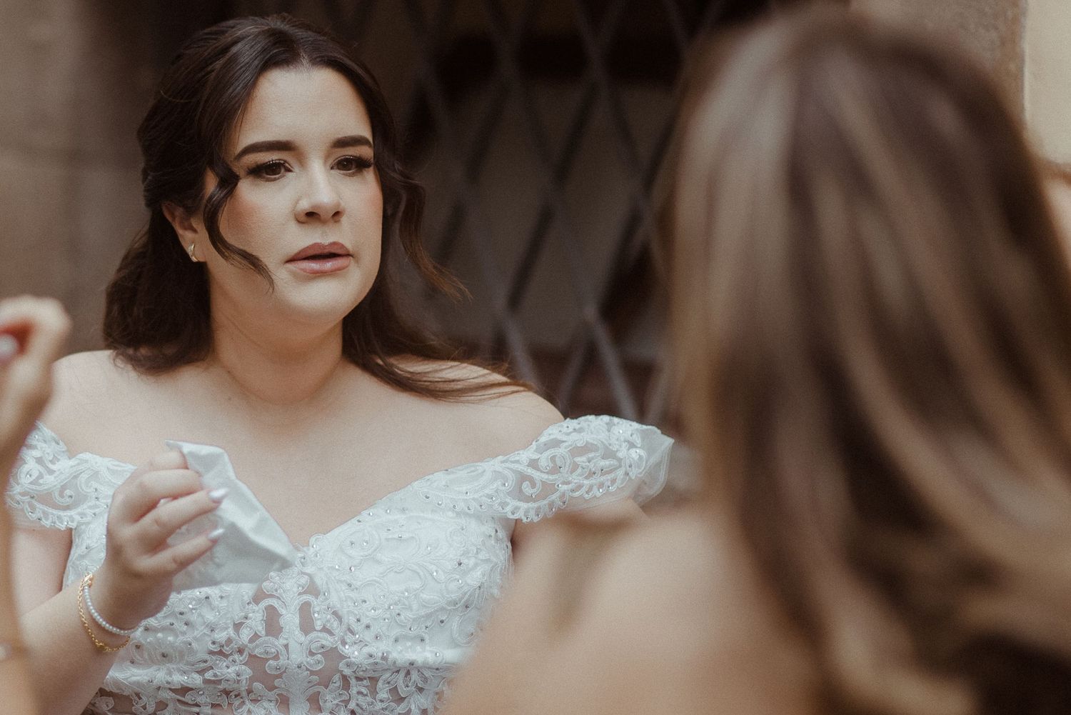 A bride in an off-shoulder lace wedding dress gets ready before the ceremony.