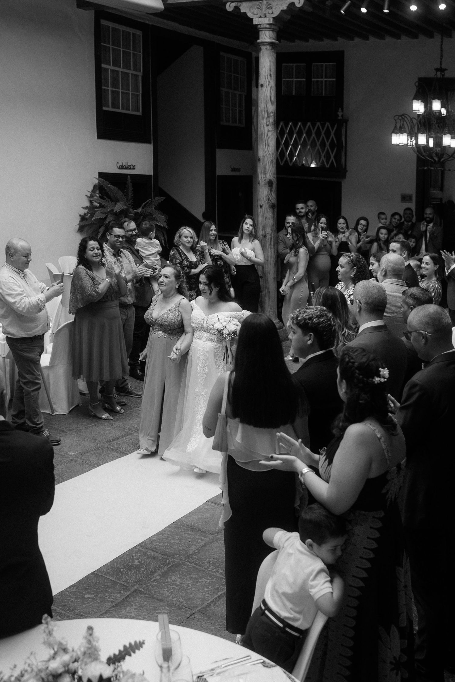 Black and white photo of a wedding celebration with guests gathered around a couple in formal attire.