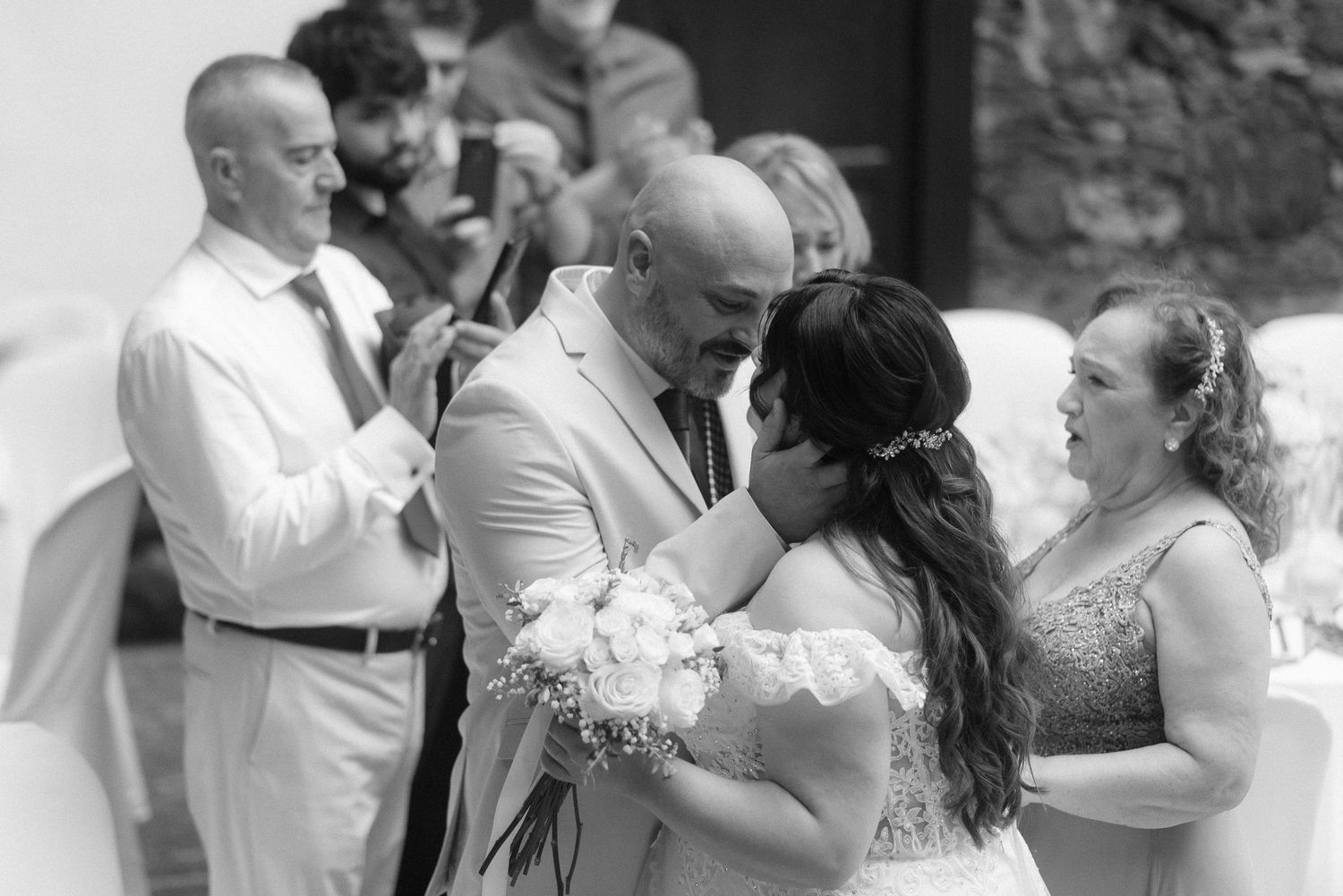 A tender moment during a outdoor wedding ceremony with attendees in white and formal attire.