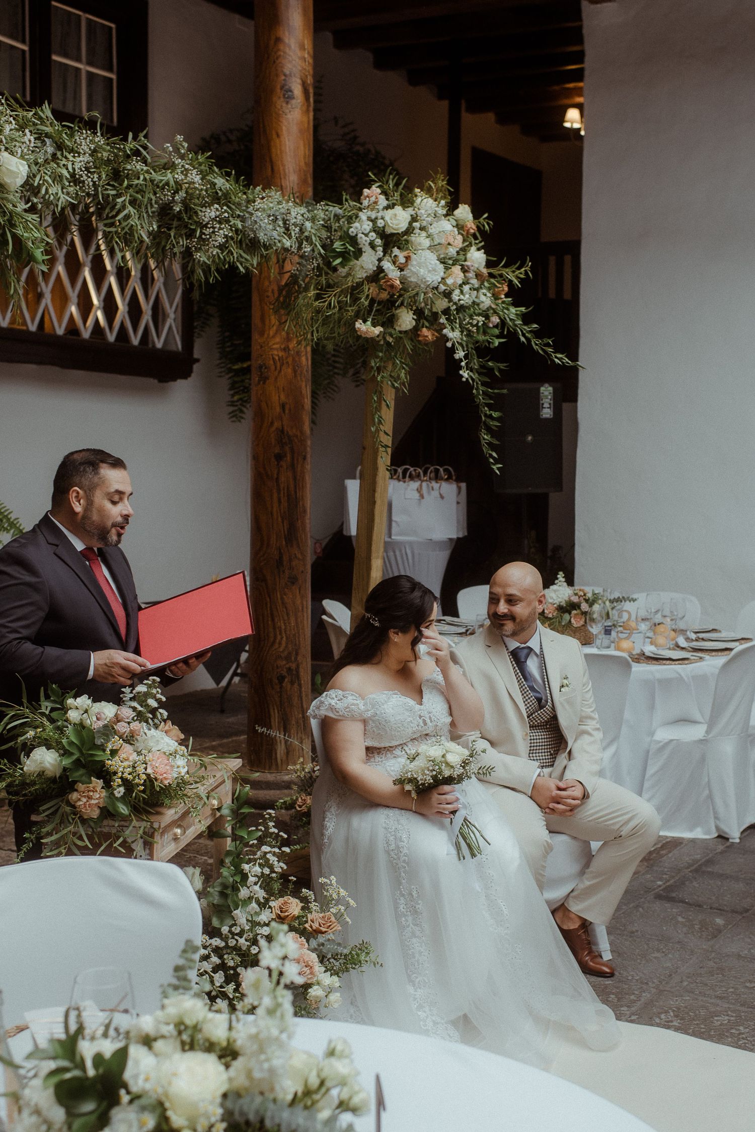 A wedding ceremony setup with elegant white floral arrangements and wooden posts in a courtyard setting.