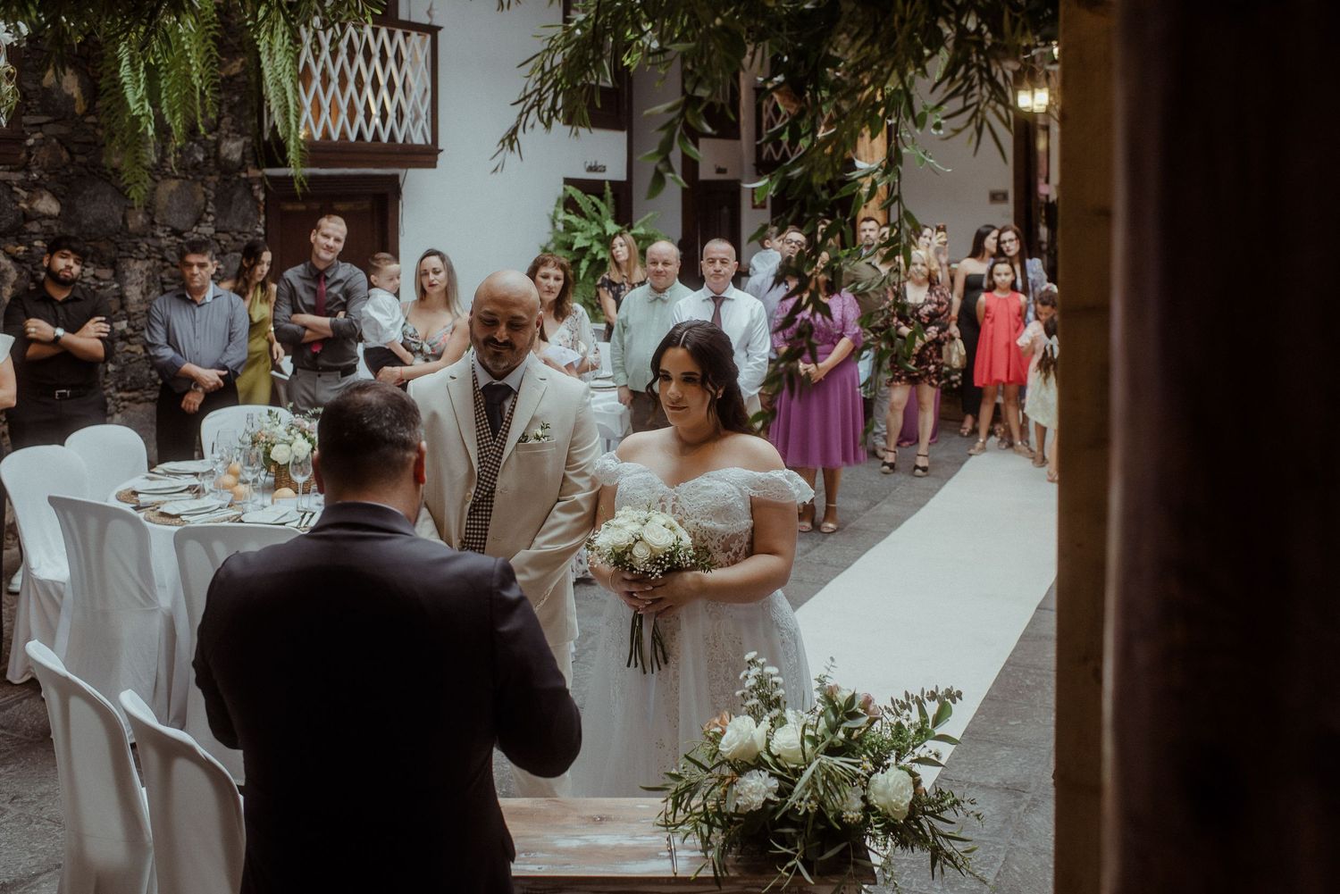 Wedding ceremony taking place in intimate courtyard setting with floral decorations and white table accents.