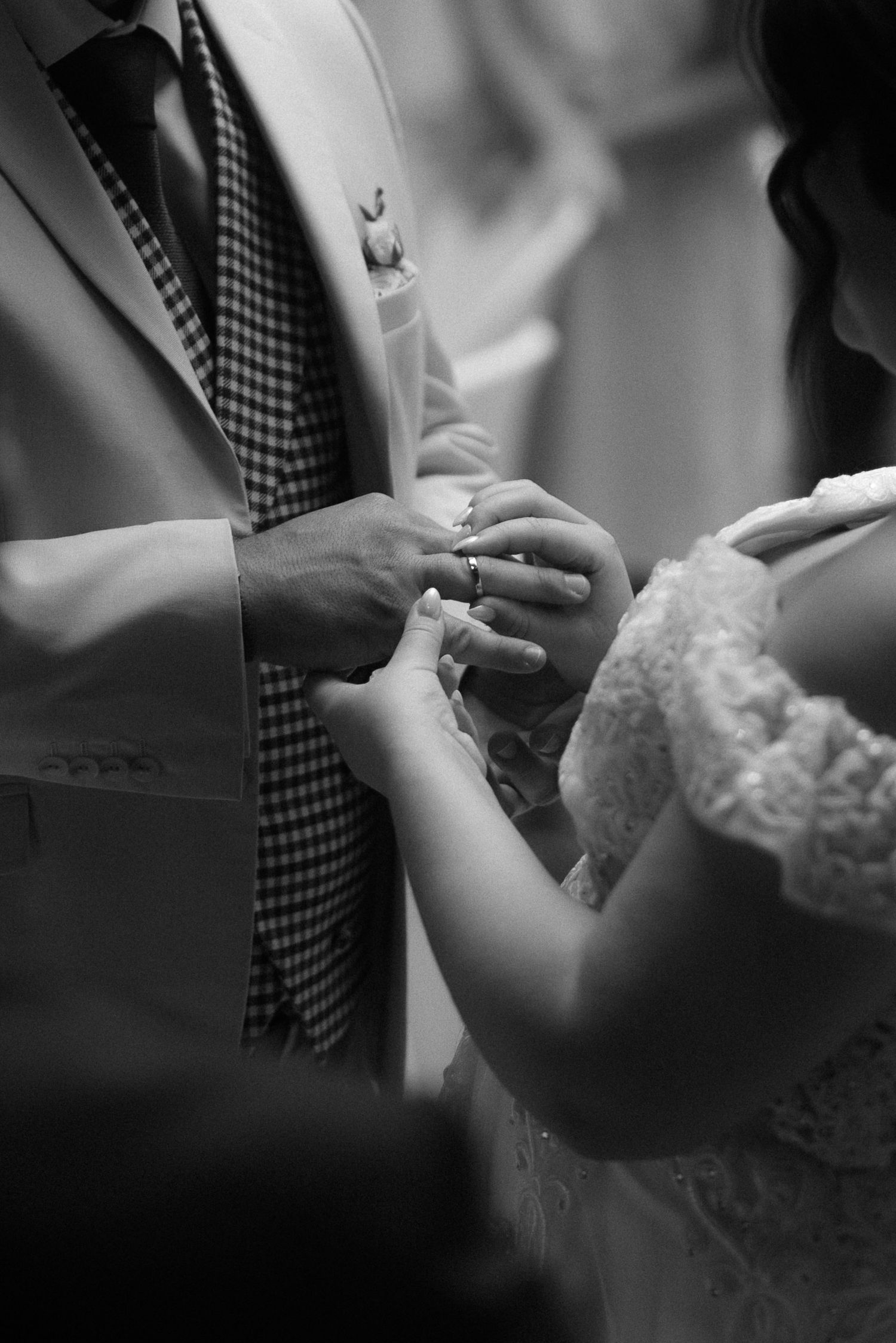 A black and white close-up photograph capturing the exchange of wedding rings during a ceremony.