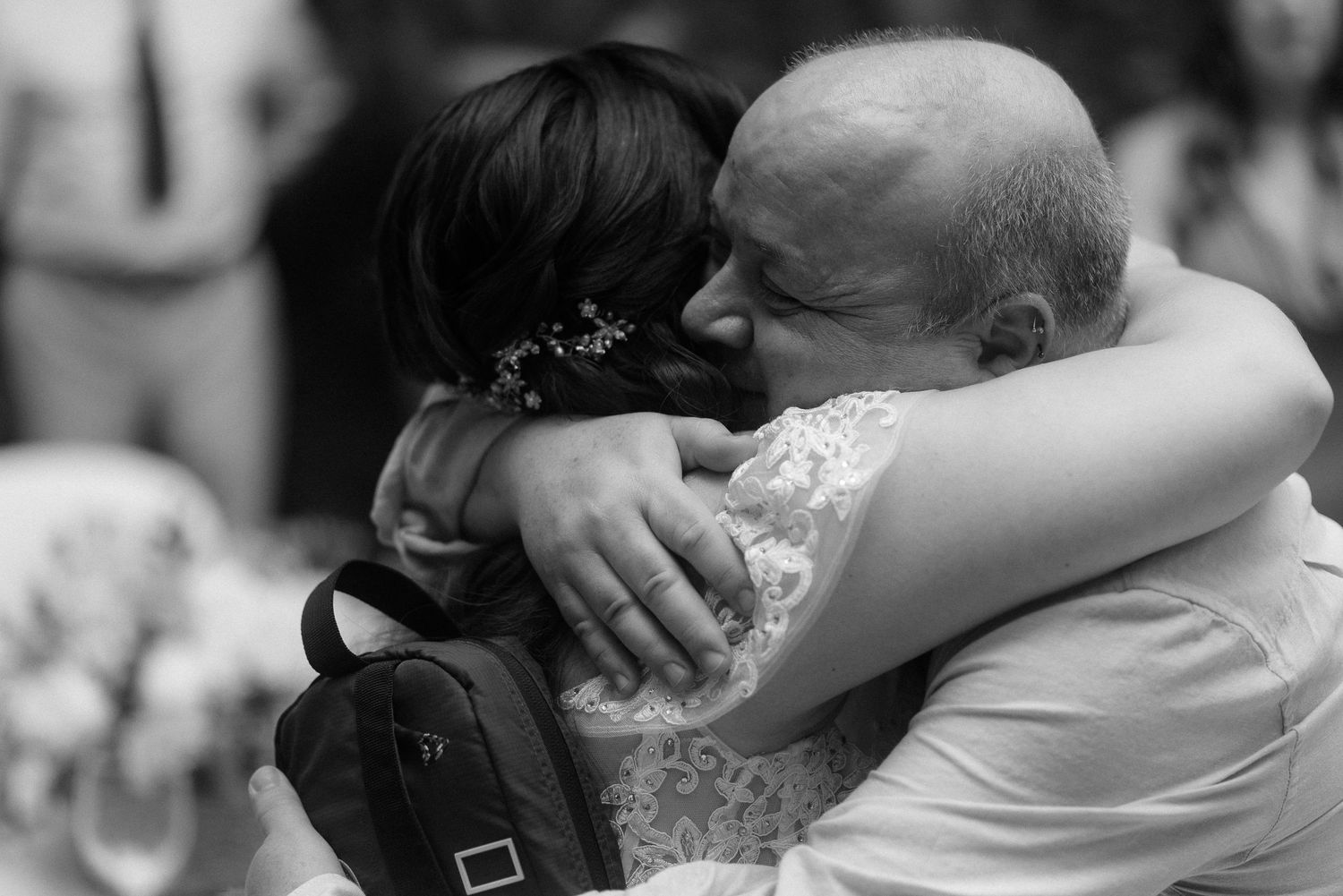 Black and white photo showing an intimate embrace between two people at what appears to be a wedding celebration.